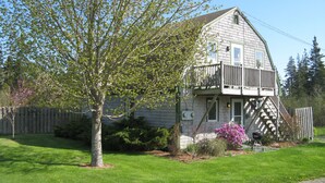 A two-story house with a balcony, surrounded by a well-maintained lawn and a wooden fence.