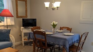 A dining area with a table set for four, surrounded by wooden chairs, a television on a stand, and a red lamp.
