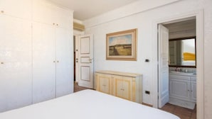 Un dormitorio con cama, armario, radiador y baño visible a través de una puerta abierta.