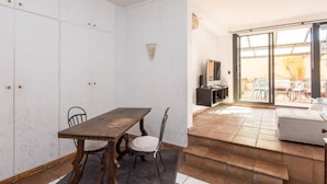 Habitación con una mesa de comedor, sillas, un televisor y un ventanal corredizo que da a un espacio exterior con sillas.