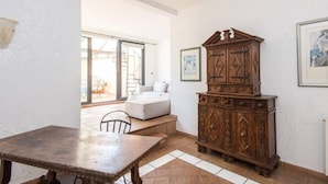 Una habitación con una mesa de madera, un armario, un sofá y un ventanal grande.