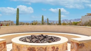 Un focolare in pietra circolare con bordatura in pietra, circondato da un'area curata con cactus e vista sulle montagne sullo sfondo.