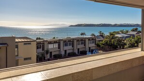 A view from a window overlooking a coastal area with buildings, palm trees, and a clear sky. - Apartment On The Beach (Waiheke Island)