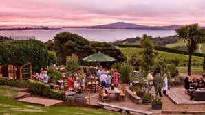 An outdoor dining area with tables and chairs, surrounded by greenery and a view of the water. - Apartment On The Beach (Waiheke Island)