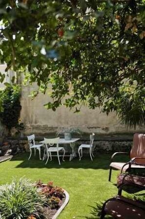 Relax under the shade of a tree in this serene outdoor seating area, surrounded by lush greenery and a beautifully manicured lawn.