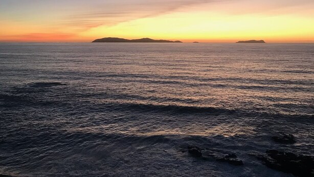 A coastal sunset view with calm sea and distant landforms.