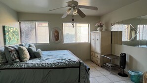 A bedroom with a bed, a ceiling fan, a window with blinds, a dresser, a mirror, and a small table. - Newly Re-decorated, 4 Recliner's Oceana, On the beach front, downtown Rosarito. (Centro Playas)