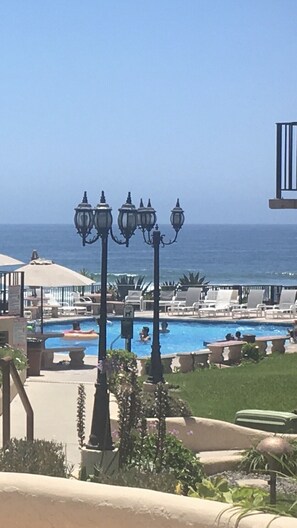 A pool area with lounge chairs and umbrellas, a lamp post, and a view of the ocean. - Downtown Rosarito Beach on beachfront Oceana condos quiet side. Best location ! (Centro Playas)
