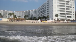 A beachfront hotel with multiple balconies, a sandy beach, and thatched umbrellas. - Villa Magna 1 Bedroom Tower 3 on 2nd Floor Oceanfront Sleep up to 4 (Nuevo Nayarit)
