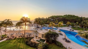 A resort pool area with multiple swimming pools, lounge chairs, and palm trees.