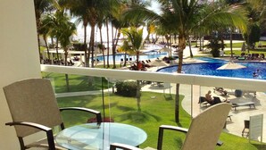 A balcony with a glass table and chairs overlooking a pool area with palm trees and lounge chairs. - Villa Magna 1 Bedroom Tower 3 on 2nd Floor Oceanfront Sleep up to 4 (Nuevo Nayarit)