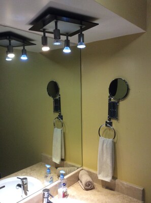 A bathroom with a sink, mirror, towel rings, and a ceiling fan.