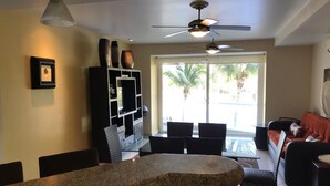 A modern living room with a dining area, a ceiling fan, and a large window with a view of palm trees. - Villa Magna 1 Bedroom Tower 3 on 2nd Floor Oceanfront Sleep up to 4 (Nuevo Nayarit)
