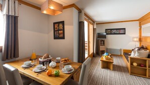 A hotel room with a dining table set for breakfast, a sofa, a TV, and a small kitchen area.