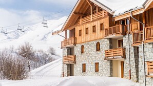 A wooden chalet with stone walls, balconies, and a ski lift in the background.