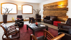 A modern living room with a wooden wall feature, leather sofas, and a red patterned rug.