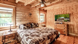 Ein Schlafzimmer in einer Holzhütte mit Bett, Kommode, Fernseher und Deckenventilator.