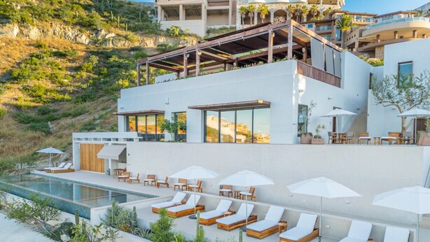 Un hôtel moderne doté d’une piscine sur le toit, de chaises longues et offrant une vue sur une colline.