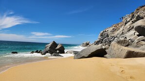 Une plage de sable avec de gros rochers et un ciel bleu dégagé.