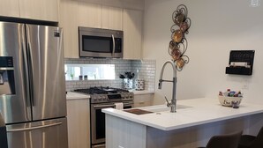 Eine moderne Küche mit Edelstahlgeräten, einer zentralen Kochinsel mit Barhocker und einem dekorativen Wandbild.