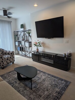 Ein modernes Wohnzimmer mit einem Flachbildfernseher, einem Sofa, einem Couchtisch, einer Zierpflanze und einem Bücherregal.