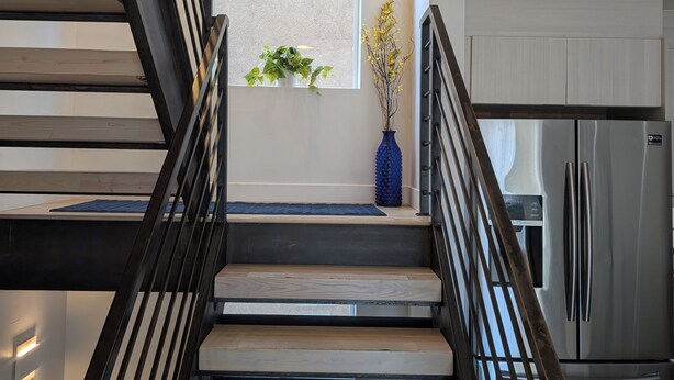 Eine moderne Treppe mit Holzboden und schwarzen Geländern, die zu einer Plattform mit einem Fenster und einer blauen Vase führt.