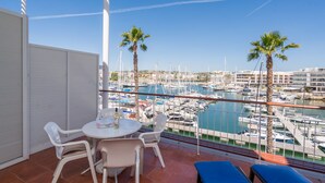 Un balcón con mesa y sillas, con vistas a un puerto deportivo con barcos y palmeras.