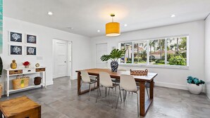 Un comedor moderno con una mesa y sillas de madera, una lámpara colgante y vistas a la vegetación a través de grandes ventanales.