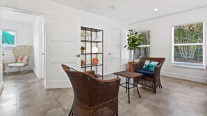 Una habitación amplia con un gran ventanal, mobiliario de mimbre y una estantería empotrada.