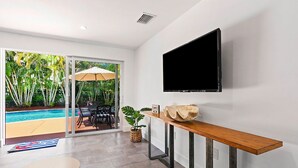 Una sala de estar moderna con un televisor montado en la pared, una mesa de centro de madera y vistas a una piscina y zona de estar al aire libre.