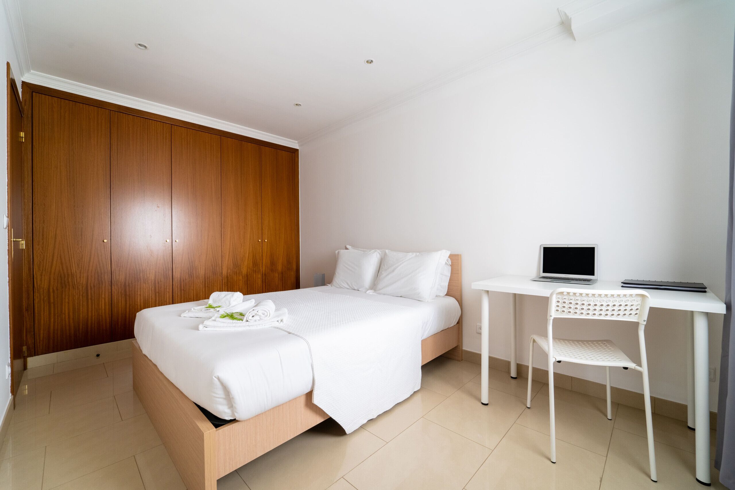 A bedroom with a bed, a desk with a laptop, and a chair.