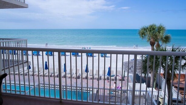 A balcony with a view of a beach, poolside chairs, and umbrellas.