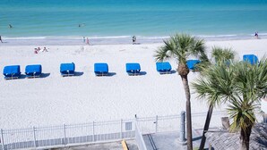 A beach with white sand and a clear blue sea. There are blue beach chairs lined up on the sand.