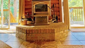 A cozy cabin interior with a wood-burning stove, large windows, and a wooden ceiling.