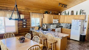 A cabin-style kitchen with wooden cabinets, a granite countertop, and a dining area with wooden chairs.