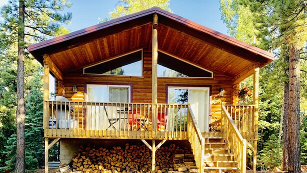 A wooden cabin with a porch, a staircase, and a stack of firewood.