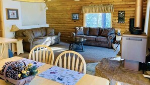 A cozy cabin interior with a dining area, two sofas, a fireplace, and a ceiling fan.
