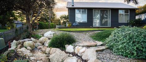 A modern house with a stone pathway leading to the entrance, surrounded by greenery and a fenced yard.