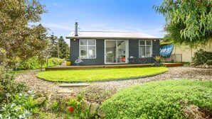 Una casa moderna con un gran ventanal corredera, un pequeño porche con mobiliario exterior y un jardín bien cuidado.