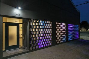 Un bâtiment avec une plaque de numéro de rue, une porte d’entrée en verre et un mur orné de panneaux lumineux.