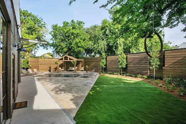 A backyard with a swimming pool, a wooden deck, and a grassy lawn.