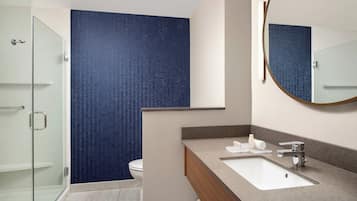 Un baño moderno con cabina de ducha de vidrio, un lavabo blanco y un espejo con marco de madera.