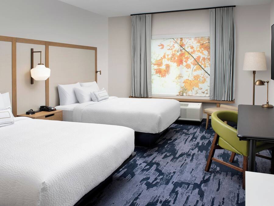 A hotel room with two beds, a desk, a chair, a lamp, and a large window with curtains.