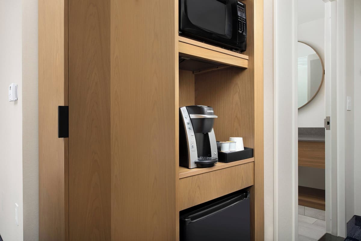 Una pequeña cocina equipada con microondas, cafetera y un refrigerador negro.