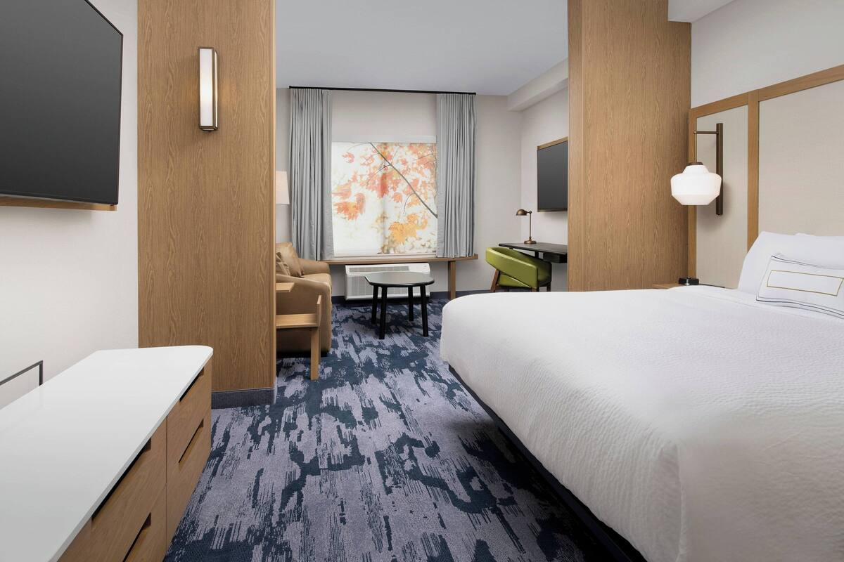 Habitación de hotel con una cama grande, un escritorio, una silla, una mesita y una ventana con cortinas.