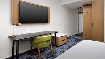 A hotel room with a bed, a desk with a chair, a wardrobe, and a flat-screen TV mounted on the wall.
