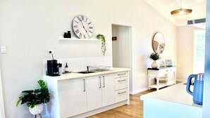 A modern kitchen with white cabinetry, a coffee machine, and a clock on the wall.
