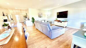 A modern living room with a grey sofa, wooden dining table, and a kitchen in the background.