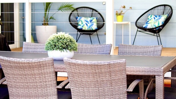 A patio with wicker furniture, a potted plant, and a small table.