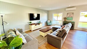 A spacious living room with a large flat-screen TV, a sofa set, a coffee table, and a side table.